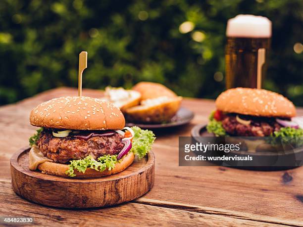 huge gourmet cheese burgers on a rustic wooden table outdoors - beer and food stock pictures, royalty-free photos & images