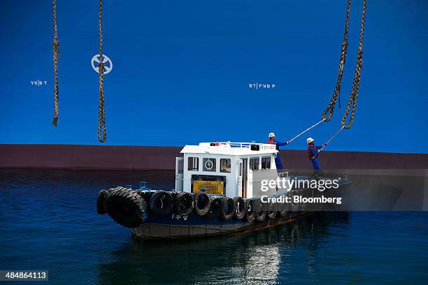 Workers on a tug boat use billhooks to catch mooring ropes from the Tangguh Palung liquefied natural gas tanker, operated by Tangguh LNG, as it...