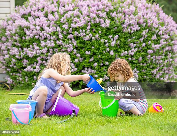 two young girls playing with garden hose and water buckets - flower bucket stock pictures, royalty-free photos & images