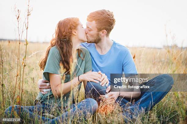first love: teenage couple kissing in meadow - tiener koppel stockfoto's en -beelden