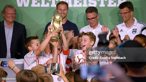 Kids celebrate with the trophy as Benedikt Hoewedes and Helmut Sandrock look on during the closing event of the 'DFB Ehrenrunde' on August 23, 2015...