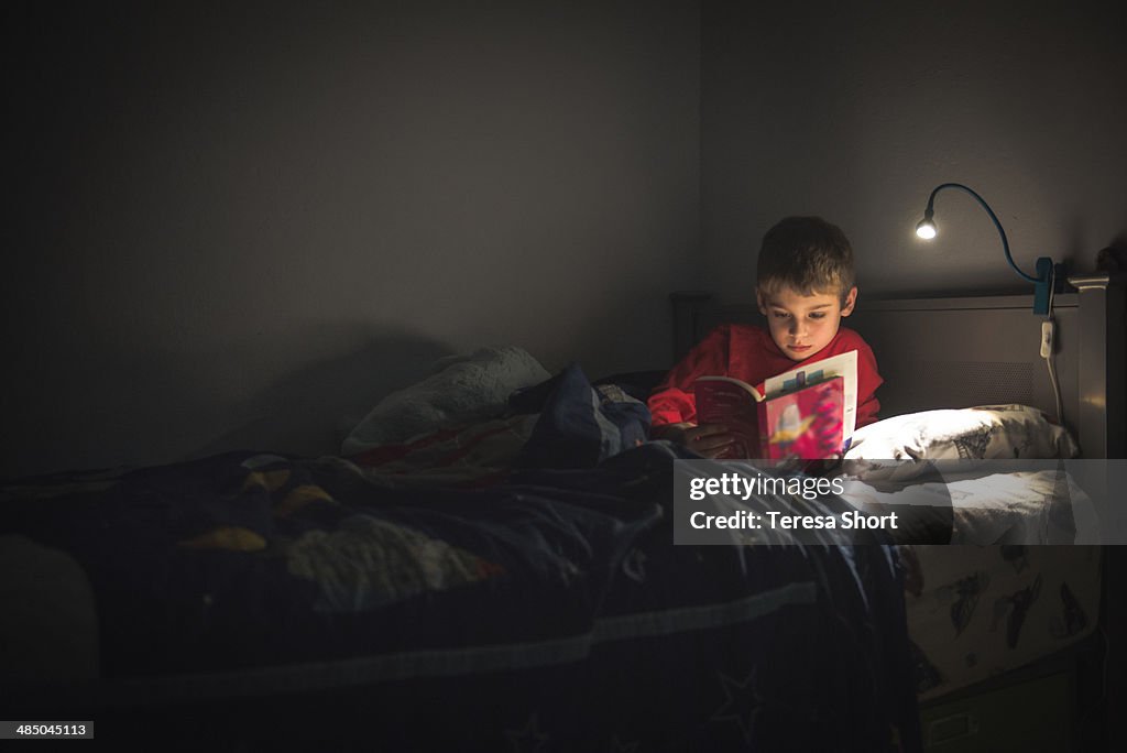 Boy reading in bed with reading lamp