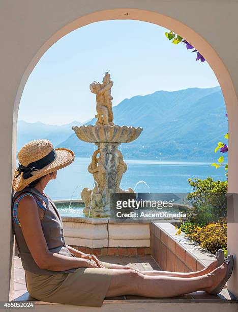woman relaxes besides fountain overlooking lake - lake maggiore stock pictures, royalty-free photos & images
