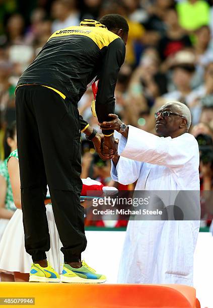 Usain Bolt of Jamaica is presented with his gold medal by outgoing president of the IAAF Lamine Diack on the podium during the medal ceremony for the...