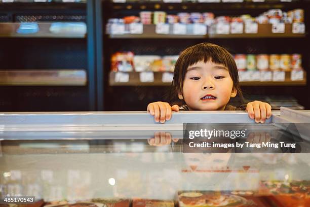 Little girl peeking into freezer in supermarket