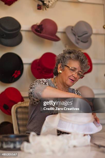 milliner attaching decoration to hat in shop - hat maker stock pictures, royalty-free photos & images