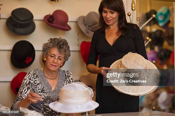 milliner adjusting hat for customer in shop - modista foto e immagini stock