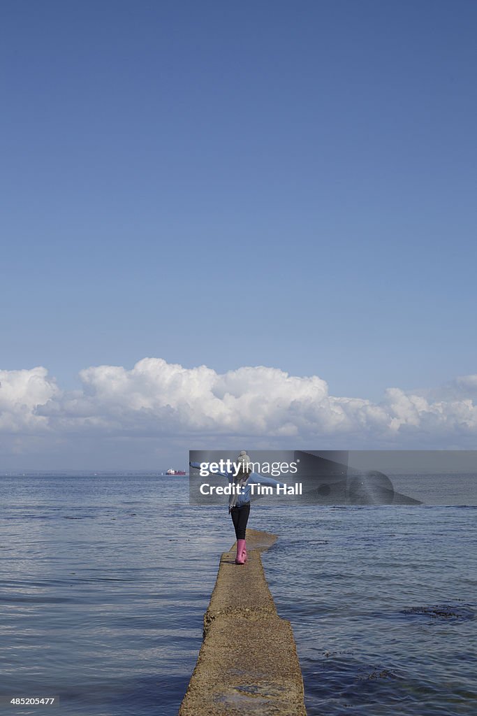 Girl walking along narrow pier at coast