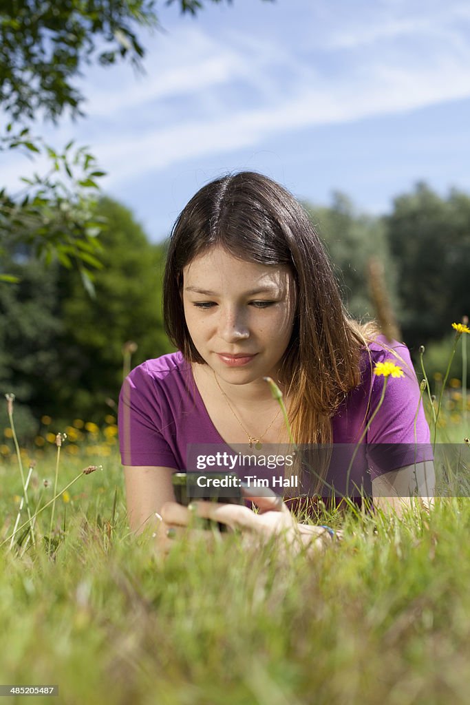 Teenage girl lying in park looking at cellphone