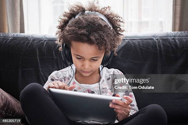 girl sitting on sofa using digital tablet and headphones - kids tablet stock-fotos und bilder