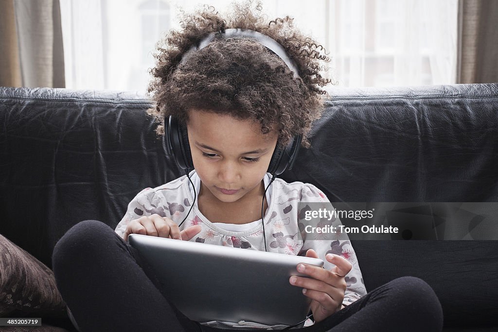 Girl sitting on sofa using digital tablet and headphones