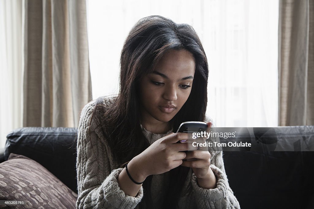 Teenage girl sitting on sofa texting on smartphone