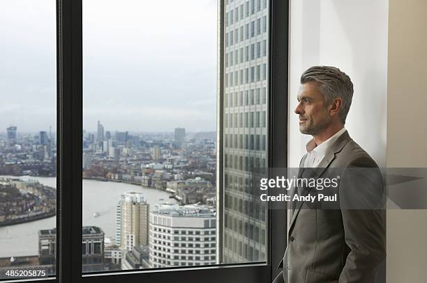 portrait of mature businessman looking out of office window, canary wharf, london, uk - rivier bos stock-fotos und bilder