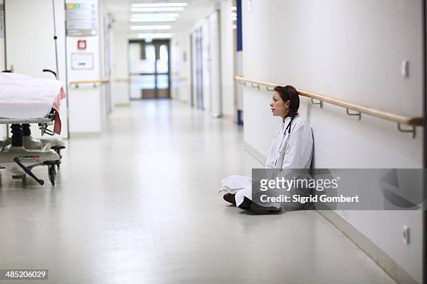 female doctor sitting cross legged in hospital corridor - sigrid gombert stock-fotos und bilder