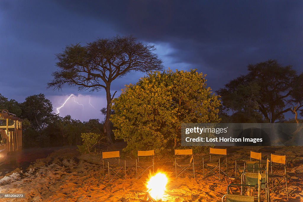 Campfire and a row of empty chairs at night, Kasane, Chobe National Park, Botswana, Africa