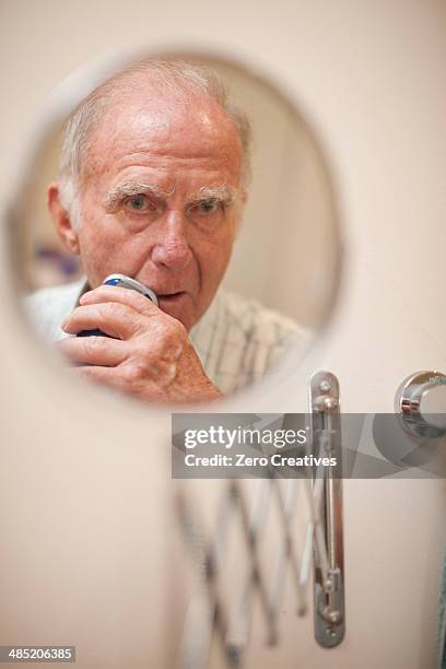 portrait of senior man in shaving mirror using electric razor - shaving foto e immagini stock