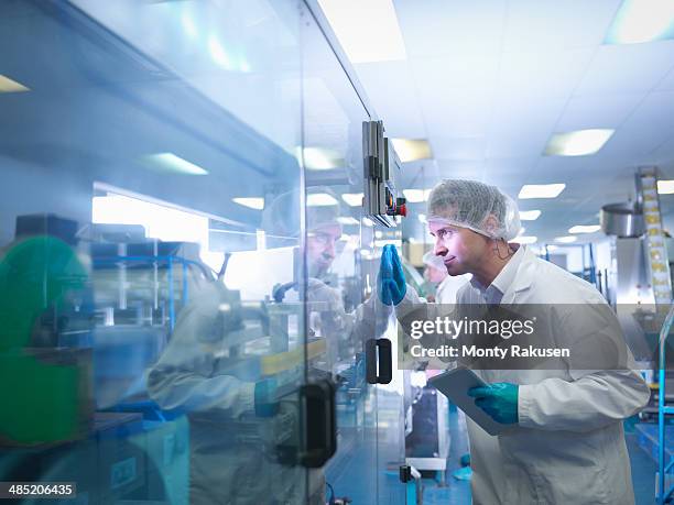 worker inspecting tablets as they are put into packaging in pharmaceutical factory - farmaceutische-fabriek stockfoto's en -beelden