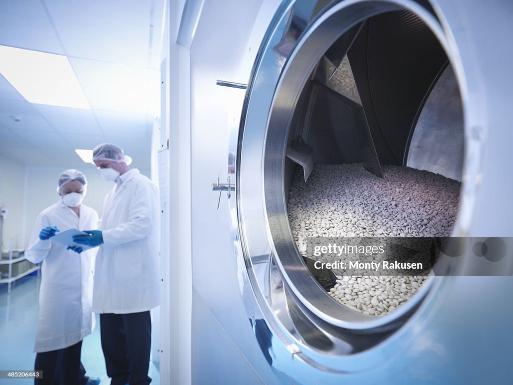 Workers with tablet coating machine in pharmaceutical factory