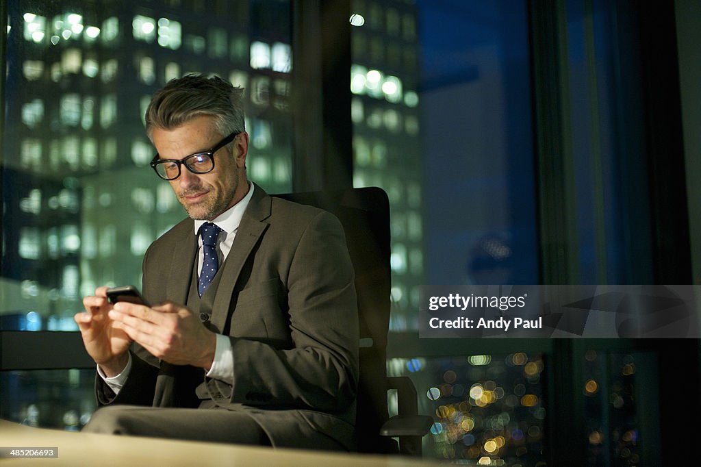 Businessman working late texting on smartphone