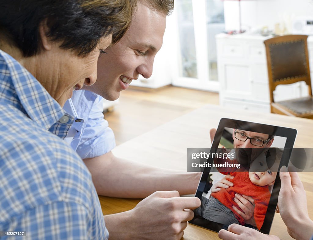 Senior woman and young man looking at image of father and baby son on digital tablet