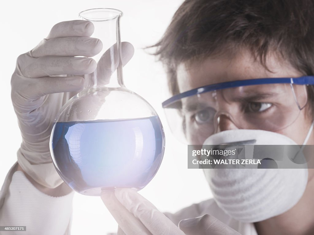 Young scientist looking at liquid in flask