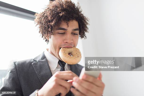young man using cell phone with bagel in mouth - ragazzo new york foto e immagini stock