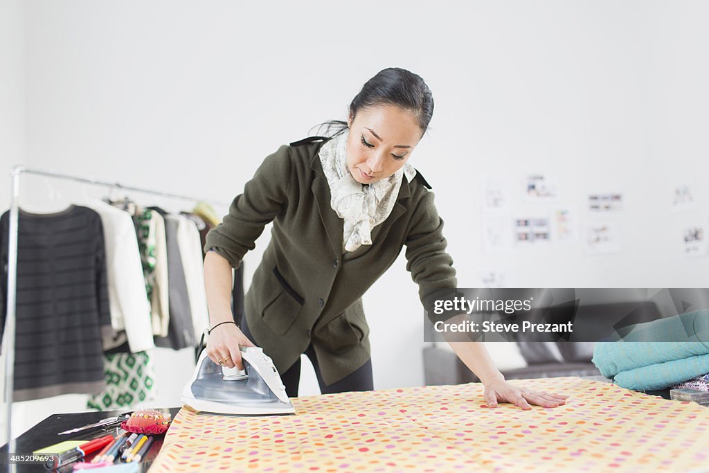 Female fashion designer ironing fabric