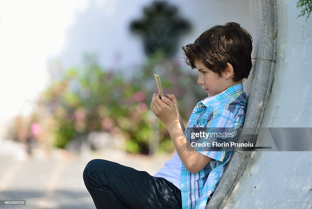 Boy leaning against curved wall texting on cellphone