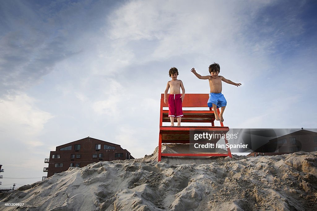 Two boys jumping off red notice board, Long Beach, New York State, USA