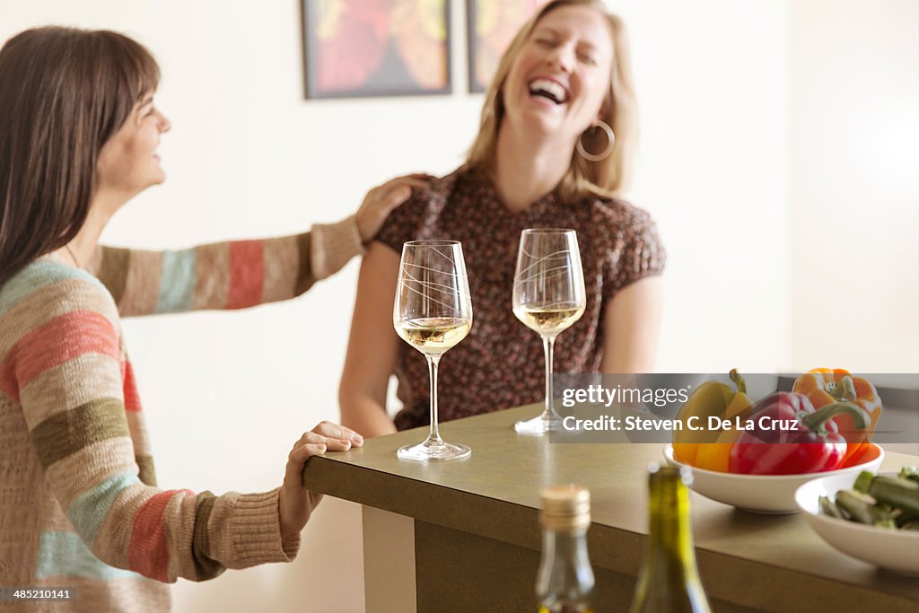 Mid adult female friends laughing in kitchen