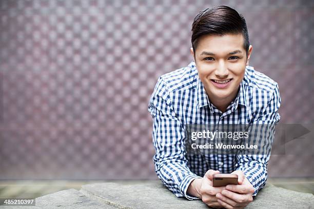 portrait of young man holding smartphone - leaning on elbows stock pictures, royalty-free photos & images