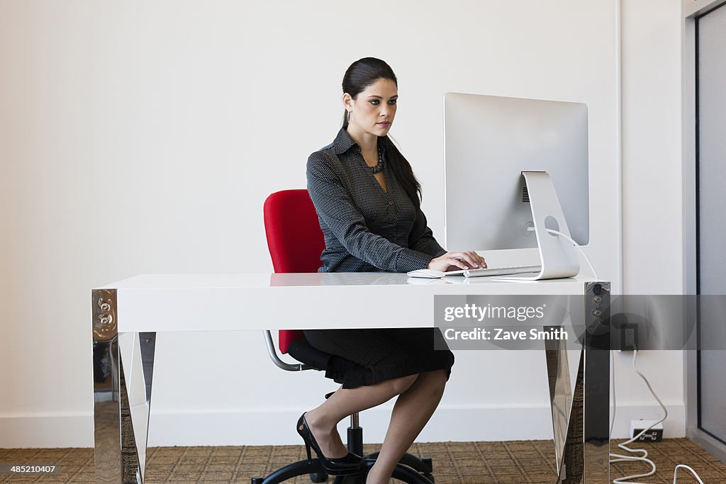 Young businesswoman sitting at desk, using computer