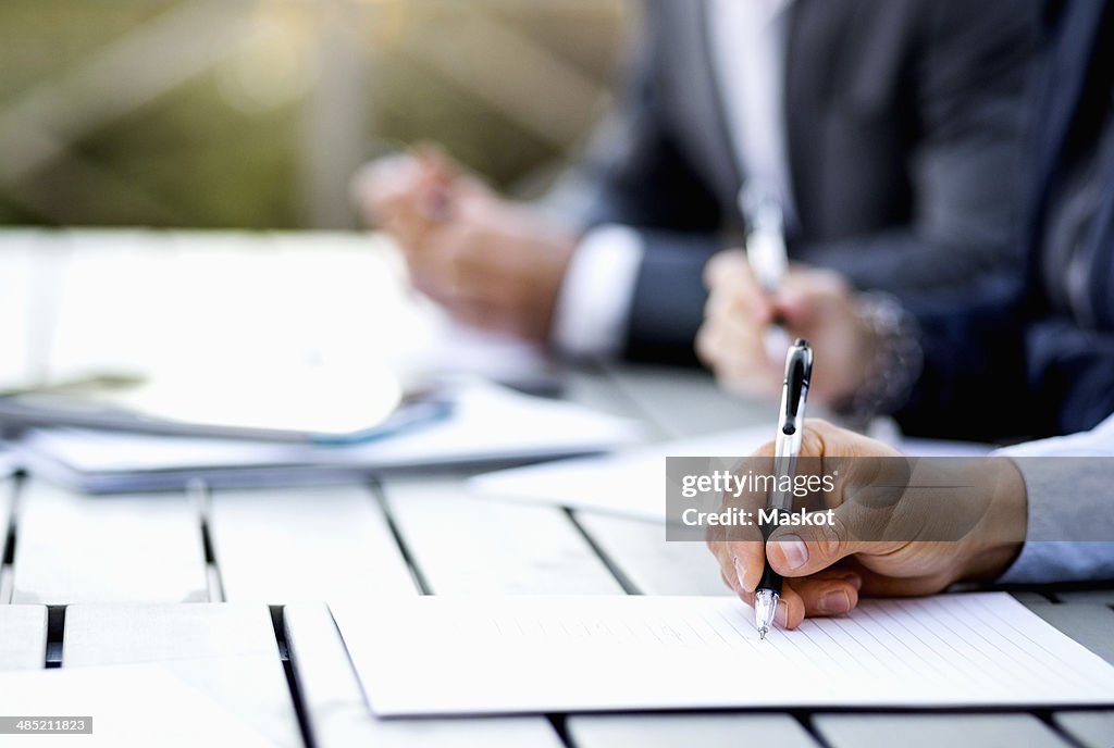 Cropped image of businessman writing on document at table
