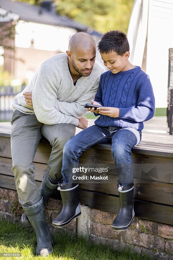 Father and son using mobile phone at yard