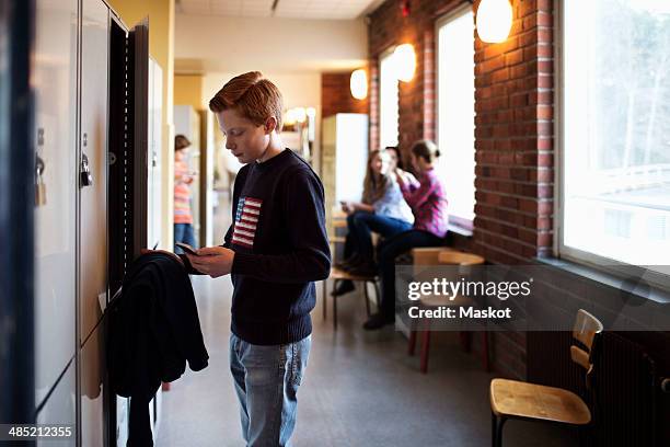 high school boy using mobile phone by locker - 12 12 12 2013 film stock-fotos und bilder