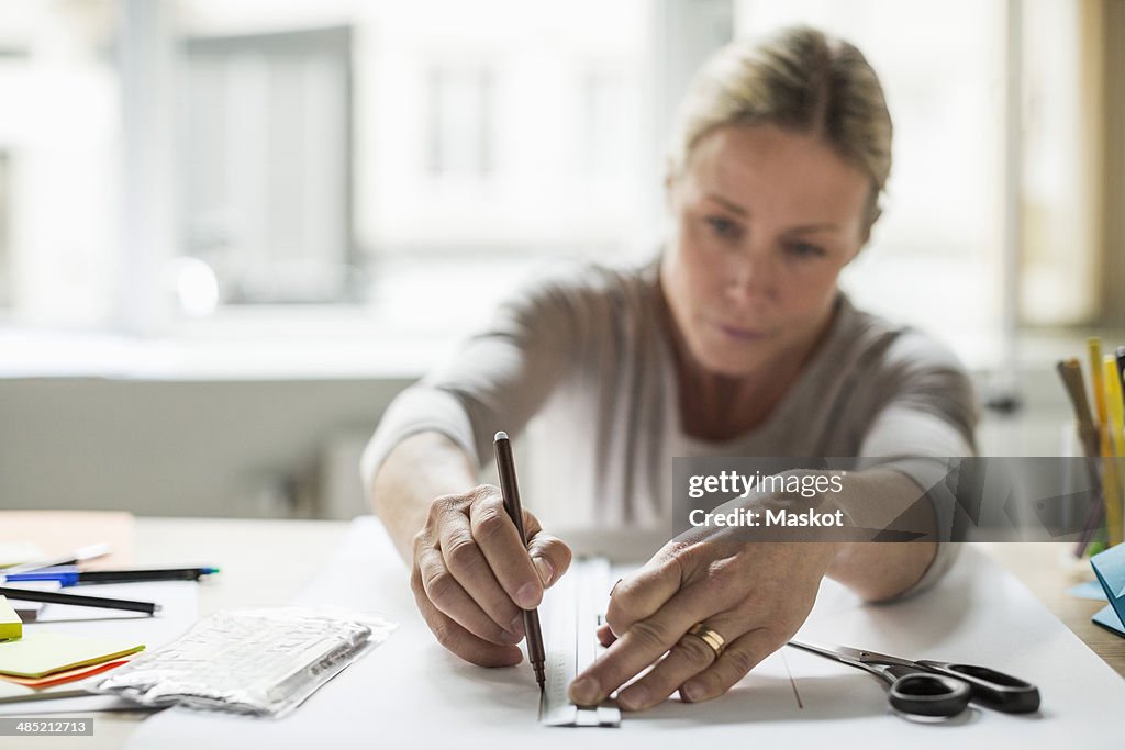 Businesswoman drawing line using ruler on paper