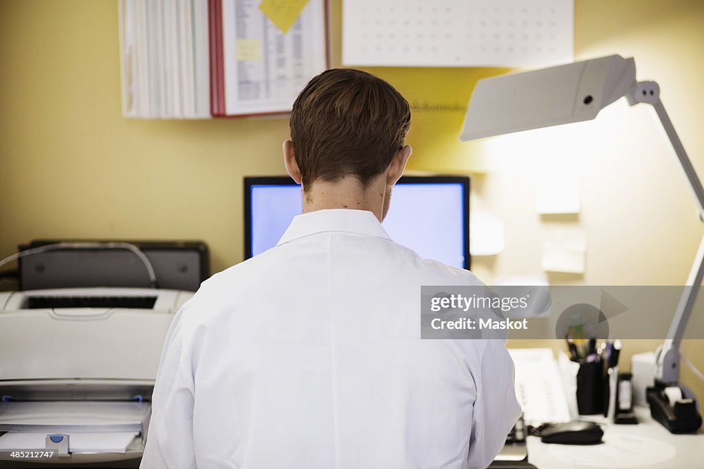 Rear view of mid adult male doctor using computer in clinic