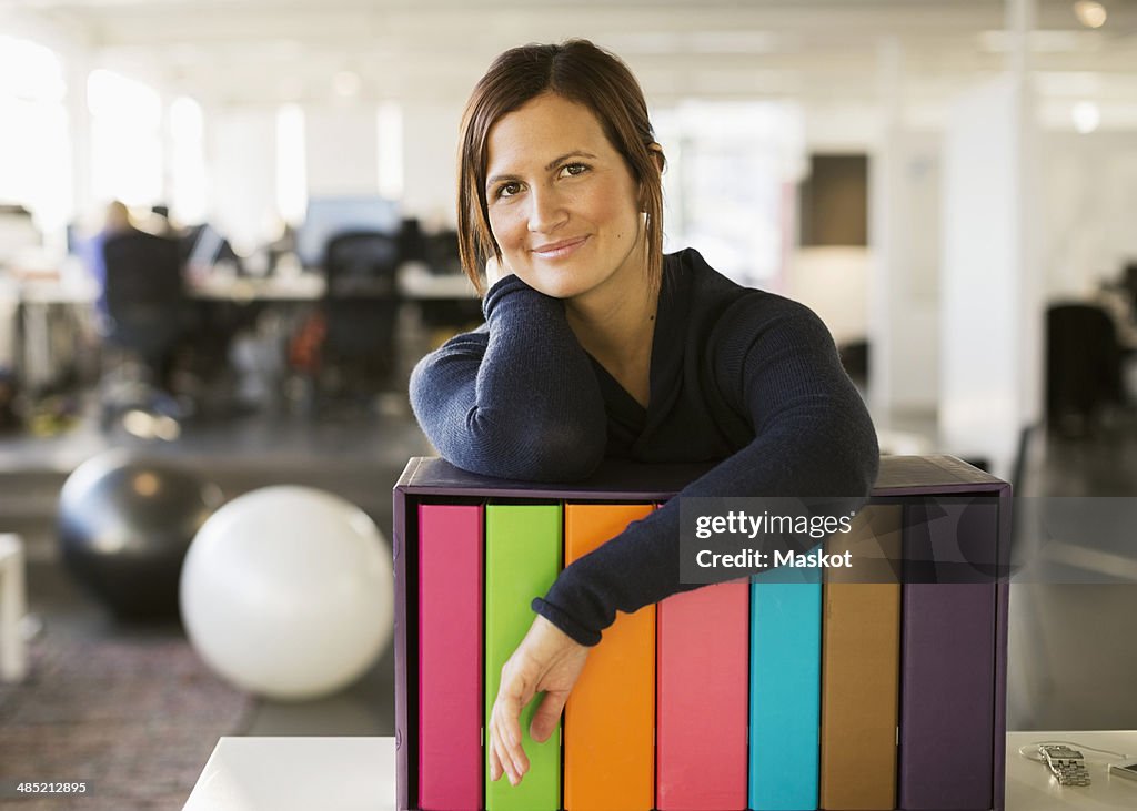 Portrait of confident businesswoman leaning on folder rack in office