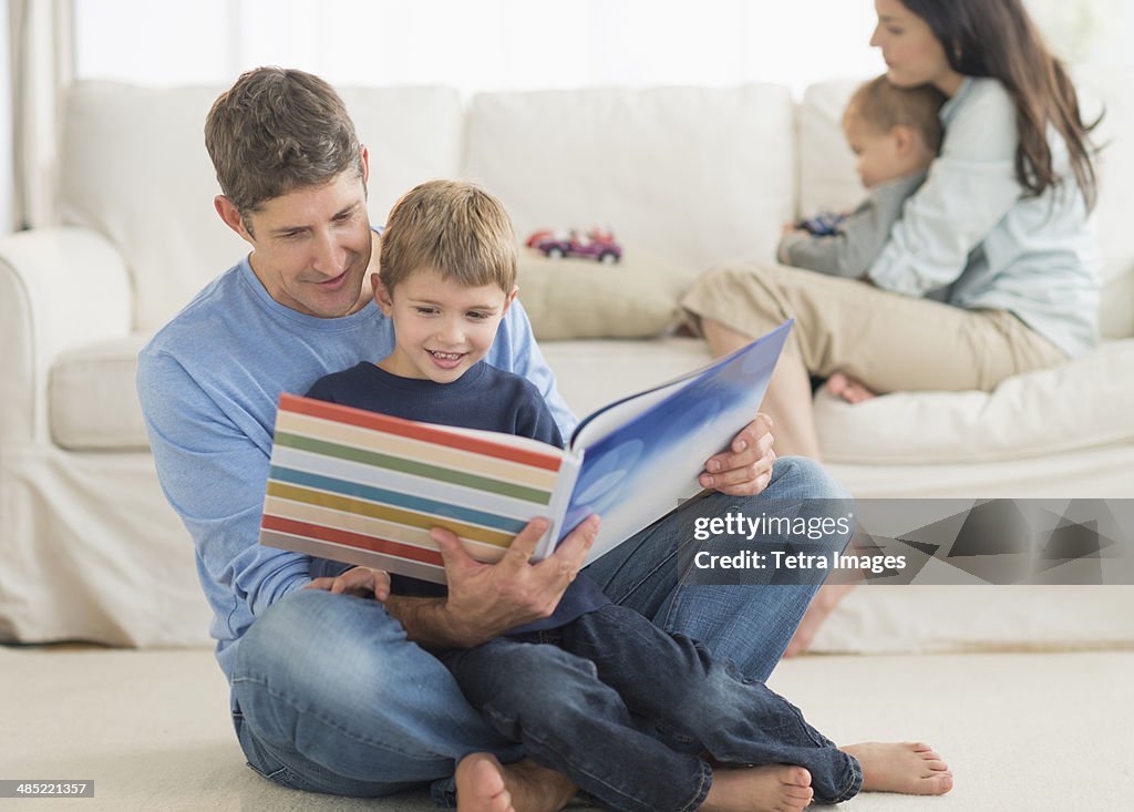 Parents with kids (12-17 months, 6-7) at home, father reading to son