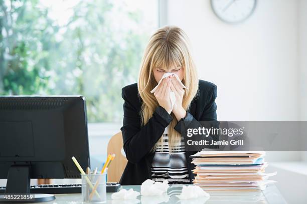 businesswoman blowing nose in office - grippe krank stock-fotos und bilder