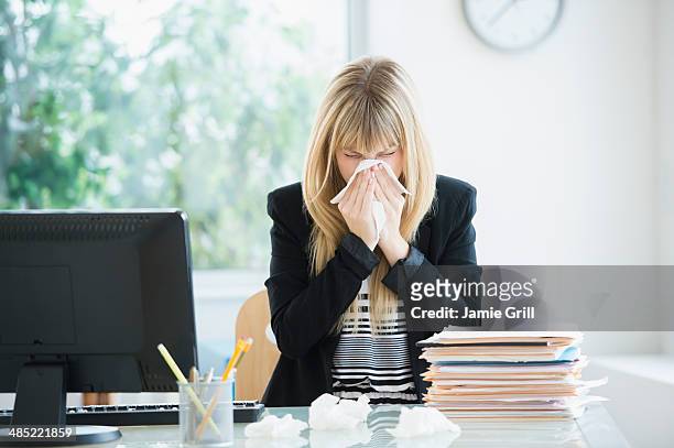 businesswoman blowing nose in office - illness stockfoto's en -beelden