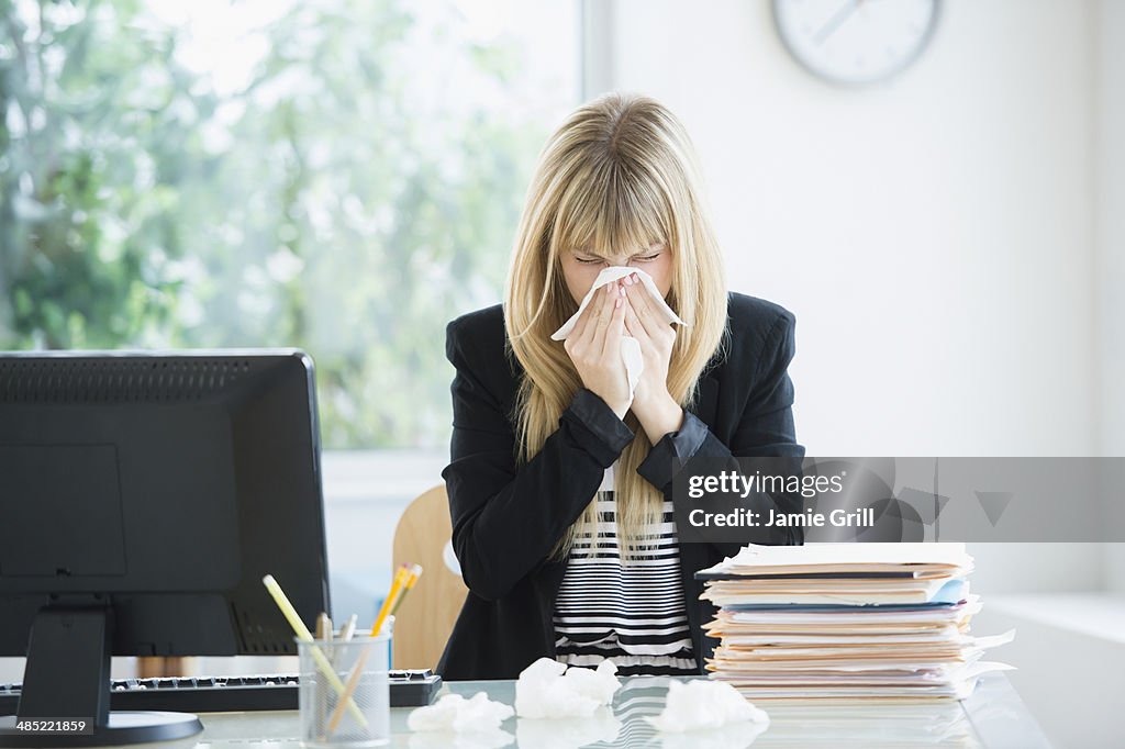 Businesswoman blowing nose in office