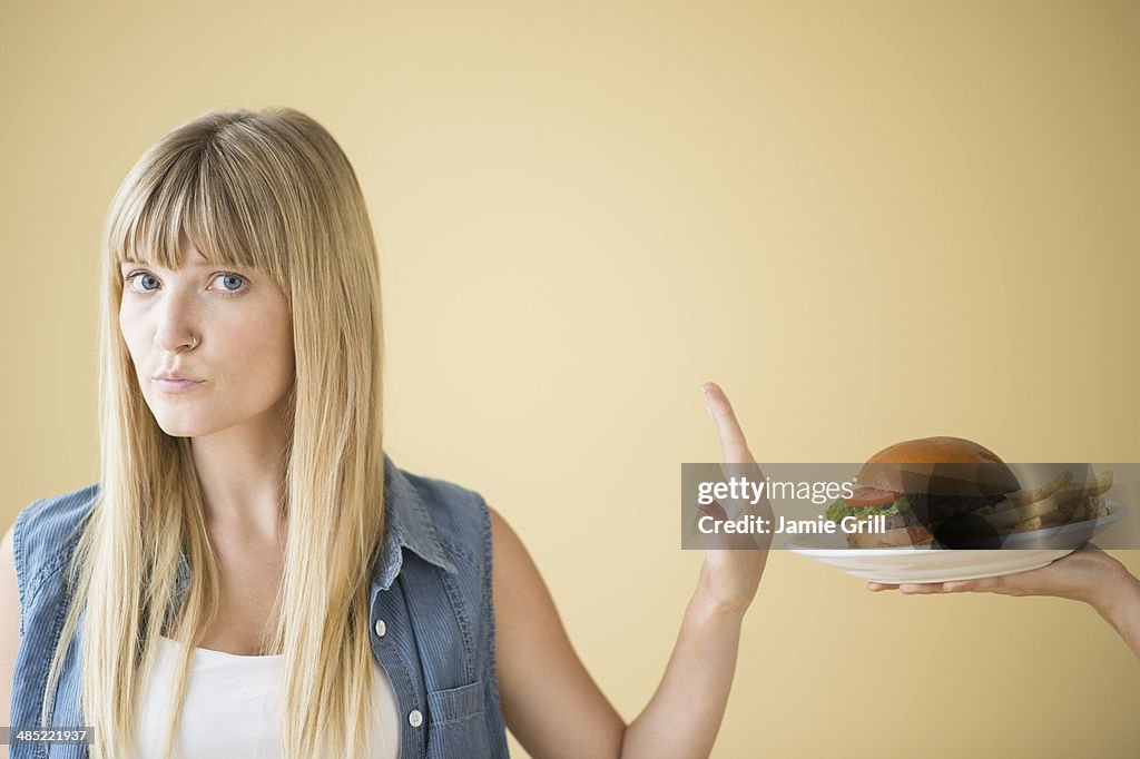 Portrait of woman rejecting hamburger that is being offered to her