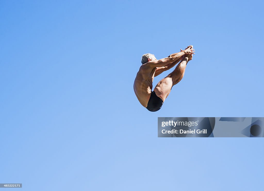 Athletic swimmer mid-air against blue sky