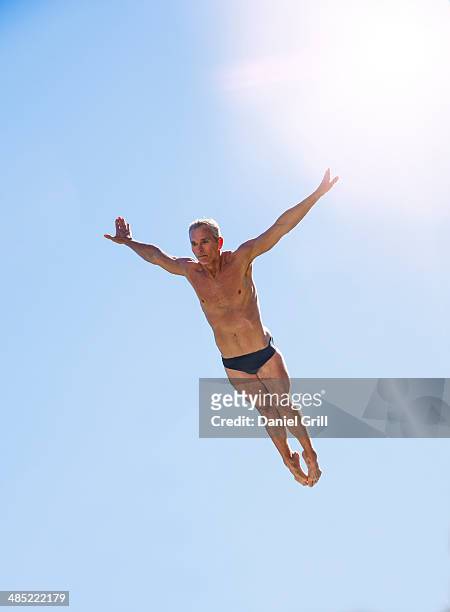 athletic swimmer mid-air against blue sky - sprungturm stock-fotos und bilder