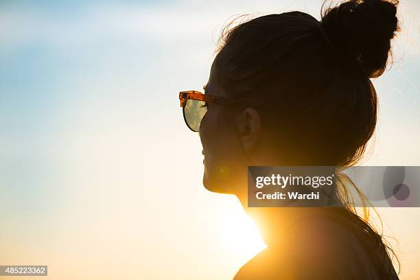 junge frau mit sonnenbrille mit blick auf den sonnenuntergang - frau mit sonnenbrille stock-fotos und bilder