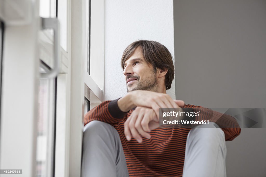 Germany, Munich, Man sitting on window sill, looking out of window