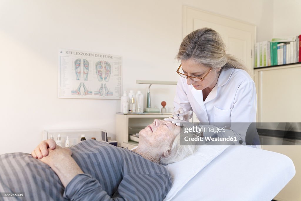 Female alternative practitioner giving senior woman injection acupuncture