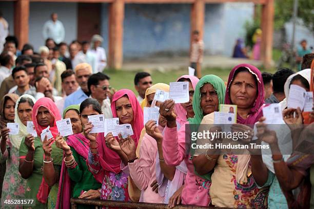 Voter showing their ID cards as they stands in a queue to cast their vote at a polling station set up inside a school at Doda on April 17, 2014 in...