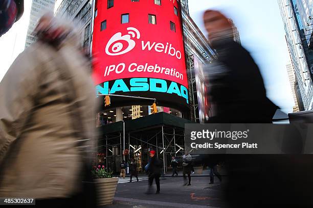 People walk by the Nasdaq exchange in Times Square moments before China's Weibo began trading on the Nasdaq exchange under the ticker symbol WB on...